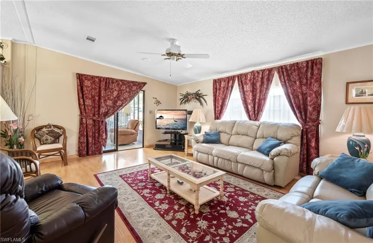 Living room with a textured ceiling, plenty of natural light, wood finished floors, and ceiling fan