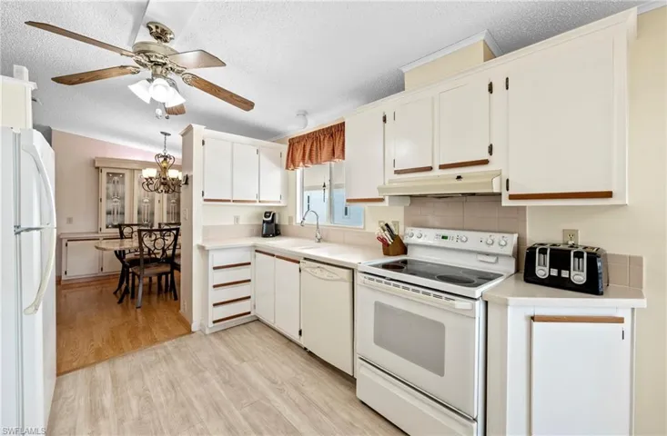 Kitchen featuring under cabinet range hood, light countertops, ceiling fan with notable chandelier, light wood-style flooring, and white appliances