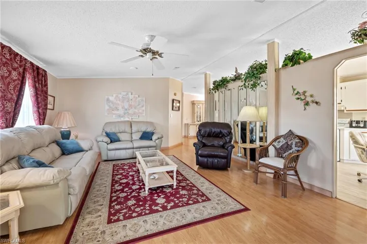 Living area with lofted ceiling, a textured ceiling, light wood-style floors, and ceiling fan