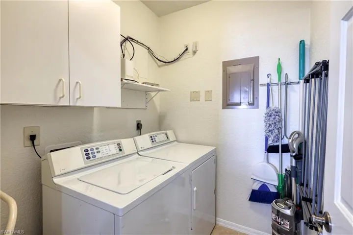 Laundry area with a textured wall, electric panel, cabinet space, and washing machine and clothes dryer