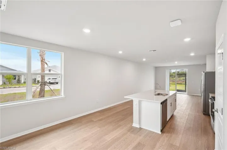 Kitchen with a kitchen island with sink, appliances with stainless steel finishes, sink, white cabinets, and light hardwood / wood-style flooring