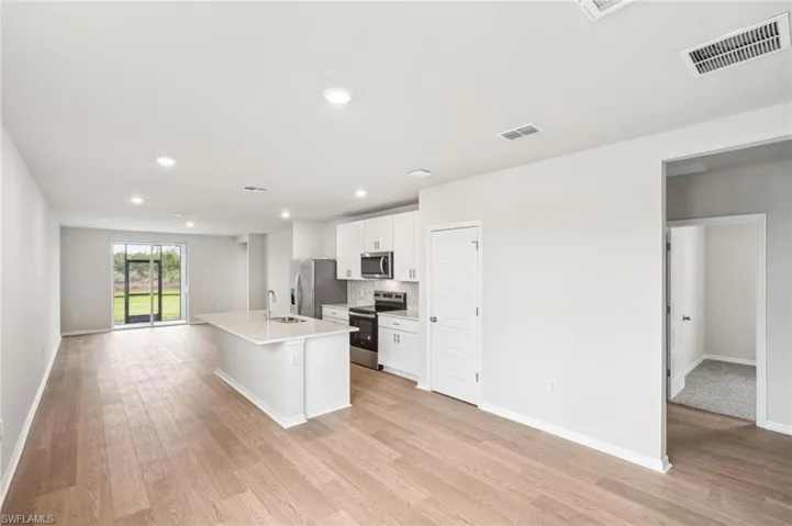 Kitchen with stainless steel appliances, white cabinetry, sink, a kitchen island with sink, and light wood-type flooring