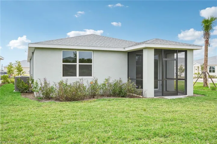Back of property with cooling unit, a lawn, and a sunroom