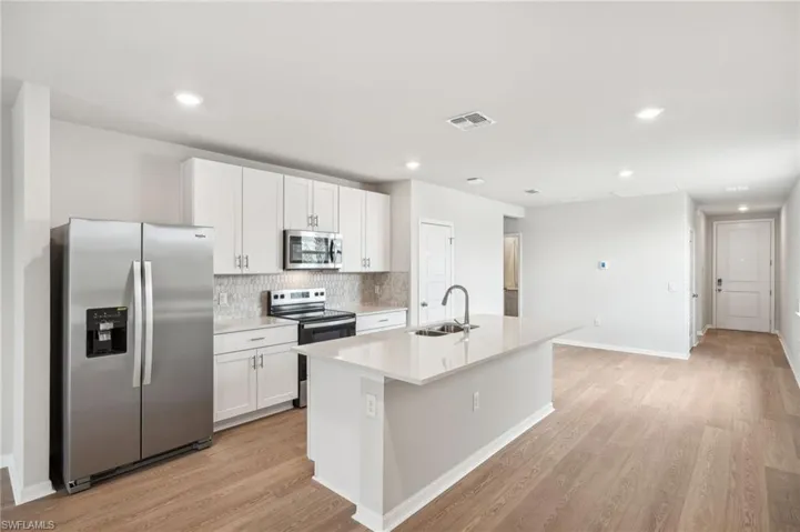 Kitchen with a kitchen island with sink, stainless steel appliances, sink, white cabinets, and light hardwood / wood-style flooring