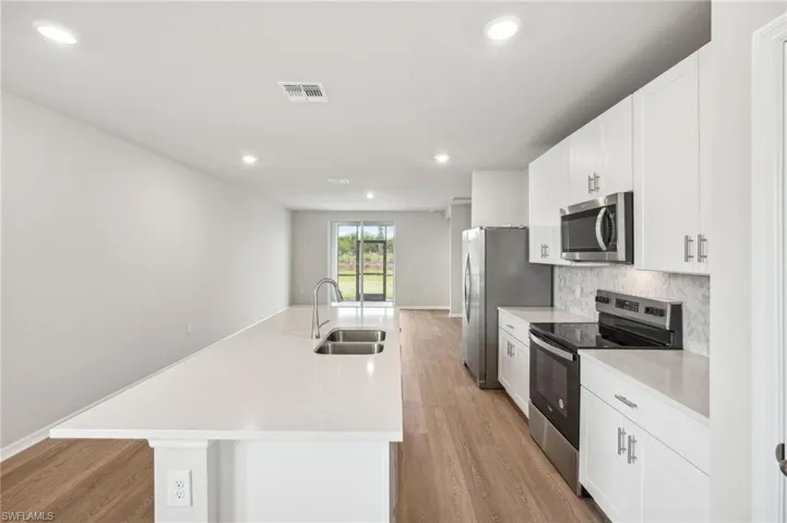 Kitchen with light wood-type flooring, appliances with stainless steel finishes, sink, an island with sink, and white cabinets