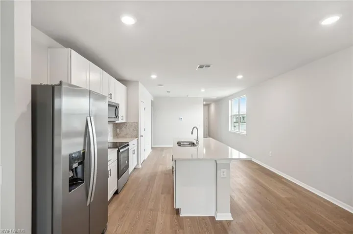 Kitchen featuring stainless steel appliances, white cabinets, sink, an island with sink, and light hardwood / wood-style flooring