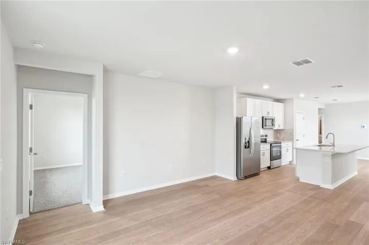 Kitchen featuring light hardwood / wood-style floors, white cabinets, sink, an island with sink, and appliances with stainless steel finishes