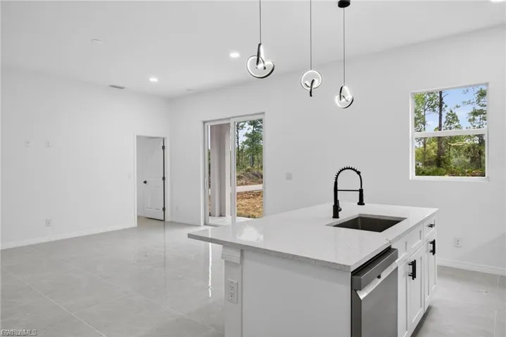 Kitchen featuring light stone counters, white cabinets, dishwasher, a center island with sink, and pendant lighting