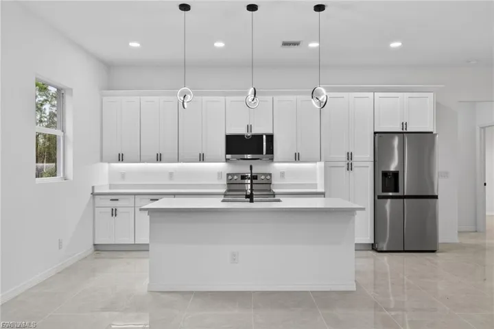 Kitchen featuring white cabinets, stainless steel appliances, light stone counters, and hanging light fixtures