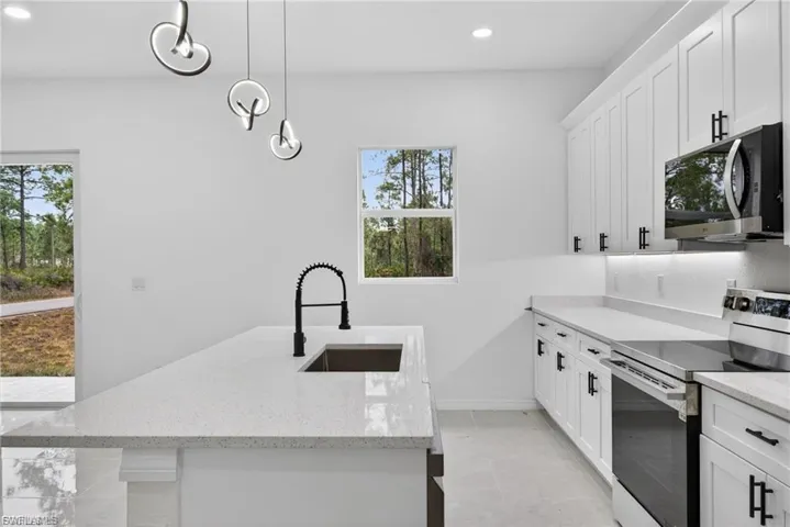 Kitchen with stainless steel appliances, an island with sink, light stone counters, decorative light fixtures, and white cabinets