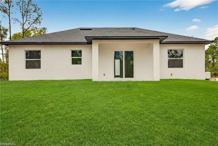 Back of property with a shingled roof, a lawn, stucco siding, and a patio