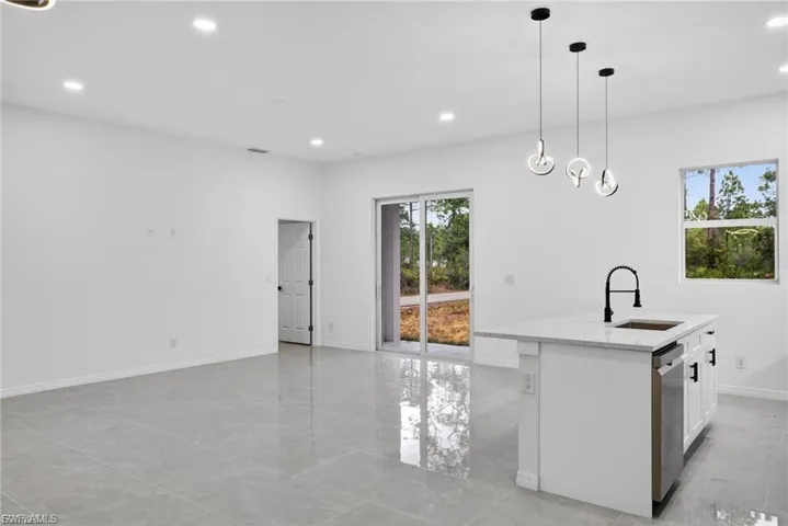 Kitchen with light stone counters, an island with sink, white cabinetry, pendant lighting, and stainless steel dishwasher