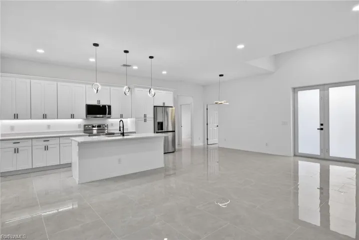 Kitchen featuring stainless steel appliances, white cabinets, an island with sink, and pendant lighting