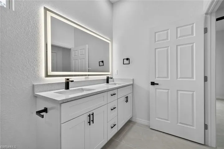 Full bathroom with double vanity, a textured wall, and light tile patterned floors