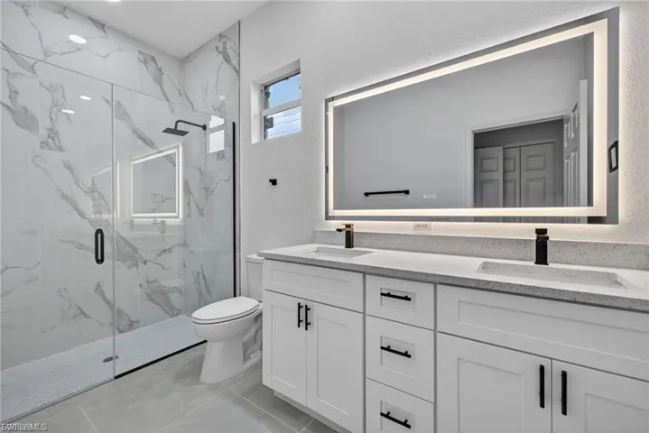 Bathroom featuring double vanity, a marble finish shower, and a textured wall