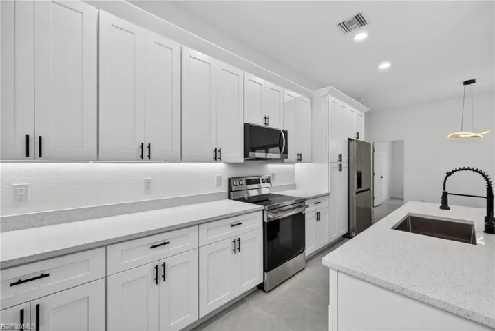 Kitchen featuring stainless steel appliances, white cabinetry, and light stone countertops