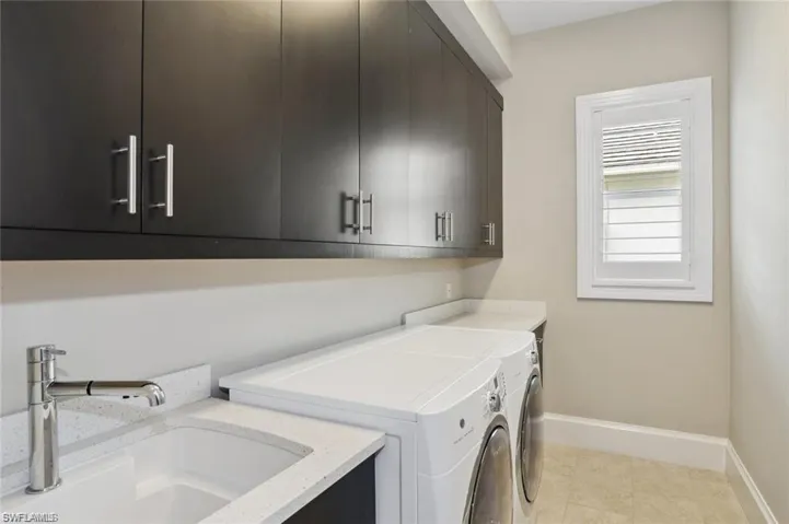 Laundry room, cabinet space, a sink, washer and clothes dryer, and baseboards