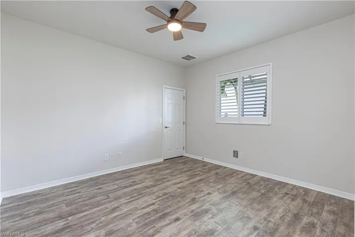 Interior room featuring wood-finish flooring, a ceiling fan with integrated lighting, and a window with white plantation shutters