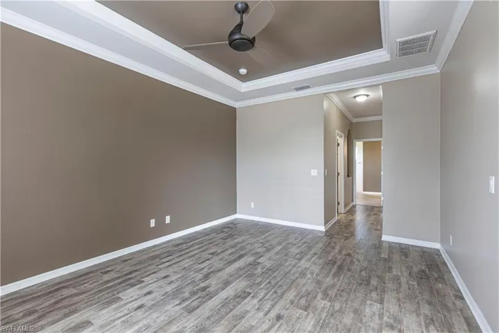 Spacious room featuring wood-finish flooring, a tray ceiling with crown molding, and a ceiling fan