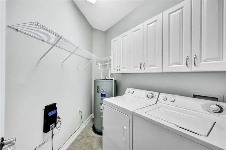 Clothes washing area with cabinets, washing machine and clothes dryer, water heater, and light tile floors