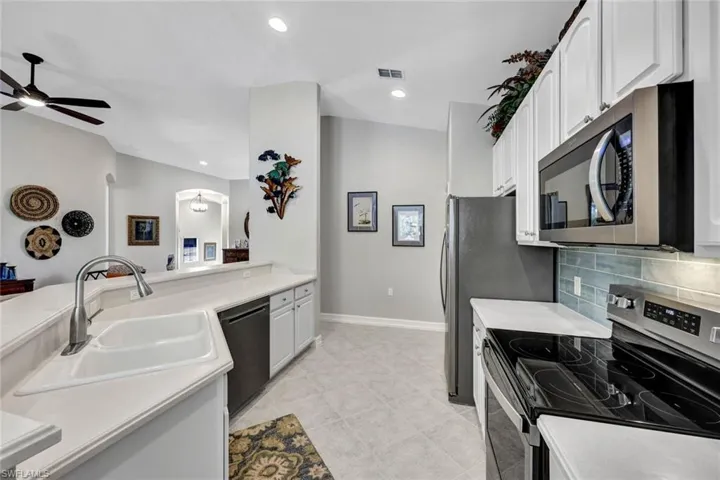Kitchen with ceiling fan, light tile floors, sink, white cabinets, and appliances with stainless steel finishes