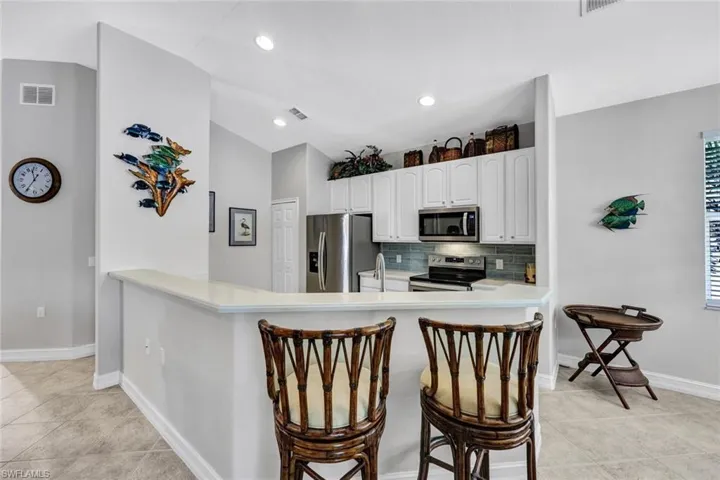 Kitchen with a kitchen breakfast bar, tasteful backsplash, stainless steel appliances, light tile flooring, and white cabinetry