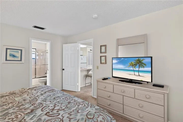 Primary bedroom featuring light carpet, a textured ceiling, freestanding refrigerator, and ensuite bath
