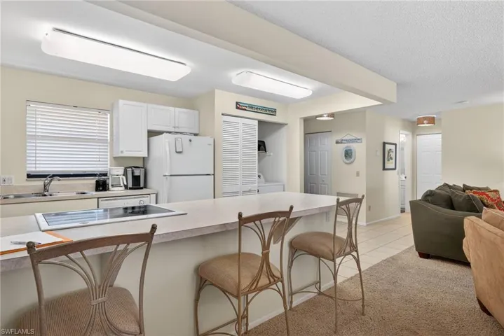 Kitchen with a breakfast bar area, light countertops, open floor plan, freestanding refrigerator, and white cabinetry