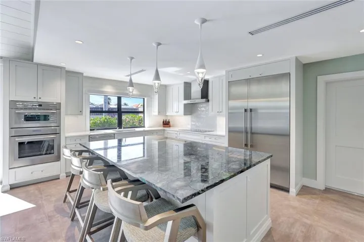 Kitchen with pendant lighting, a center island, wall chimney range hood, dark stone countertops, and appliances with stainless steel finishes