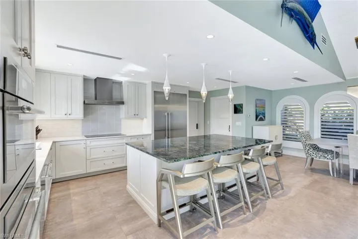Kitchen with white cabinetry, a center island, wall chimney range hood, a kitchen breakfast bar, and built in fridge