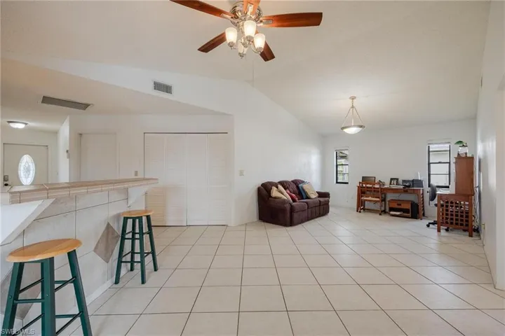Living room with vaulted ceiling, light tile patterned floors, a ceiling fan, and an office area