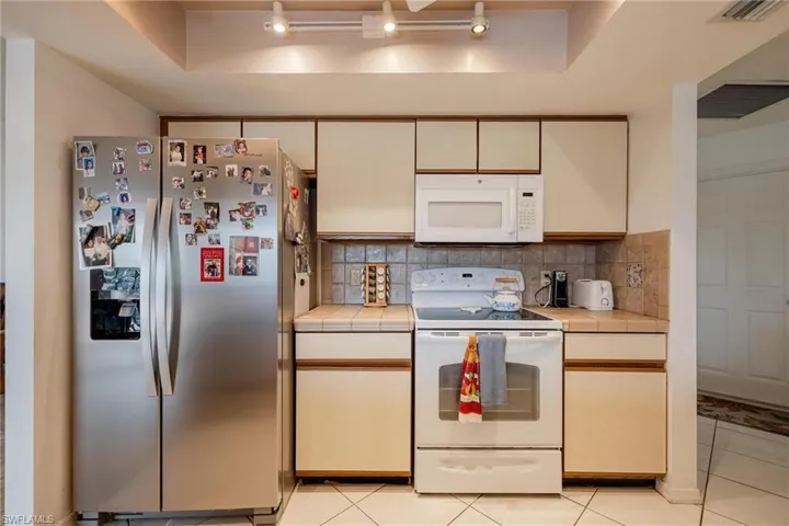 Kitchen featuring white appliances, tile counters, light tile patterned flooring, backsplash, and a tray ceiling