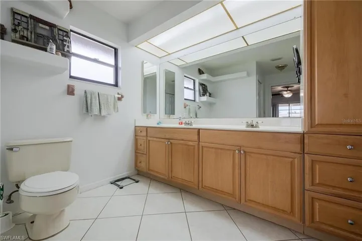 Full bathroom with double vanity, light tile patterned floors, and ceiling fan