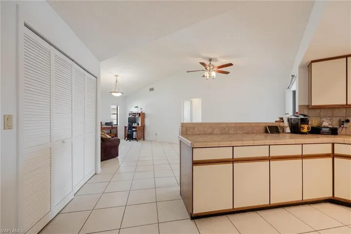 Two tone kitchen with tile countertops, backsplash, a peninsula, a ceiling fan, and lofted ceiling
