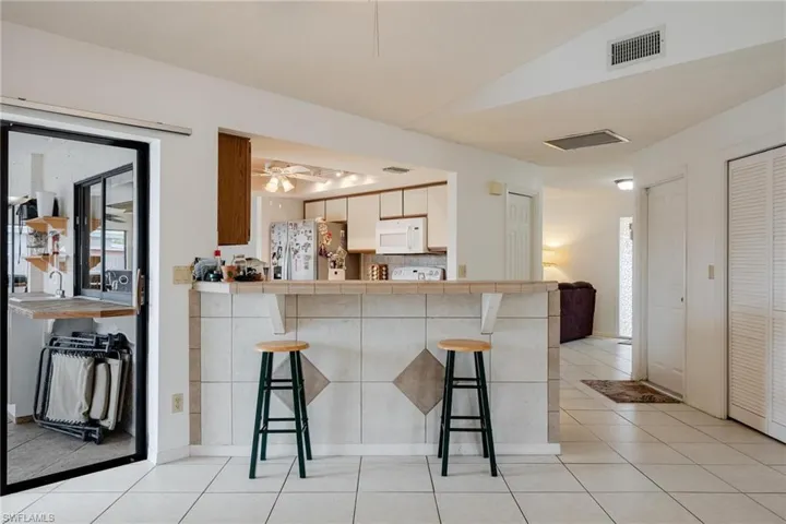 Kitchen with a breakfast bar, light tile patterned flooring, stainless steel fridge with ice dispenser, white microwave, and vaulted ceiling