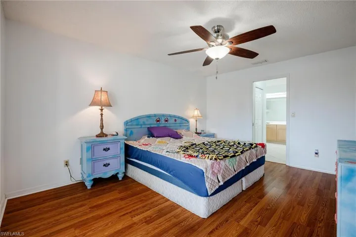 Bedroom with wood finished floors, ceiling fan, ensuite bathroom, and a textured ceiling