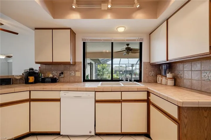 Two tone kitchen with ceiling fan, dishwasher, two tone cabinetry, tasteful backsplash, and light tile patterned floors