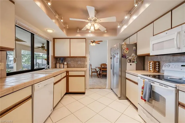 Dual tone kitchen with track lighting, white appliances, a tray ceiling, two tone cabinets, and ceiling fan