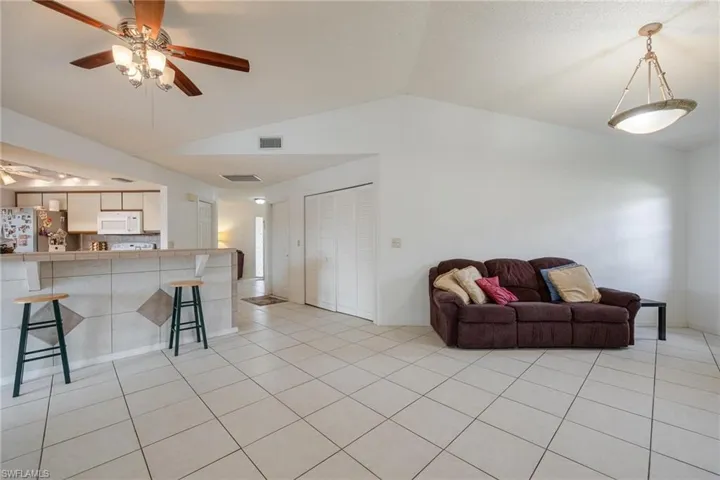 Living room featuring a ceiling fan, lofted ceiling, and light tile patterned flooring