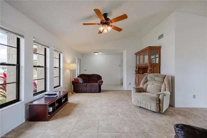 Living room with lofted ceiling, ceiling fan, and light tile patterned floors