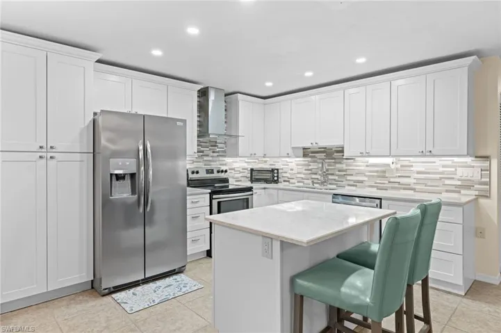 Kitchen featuring appliances with stainless steel finishes, a center island, wall chimney range hood, and white cabinets