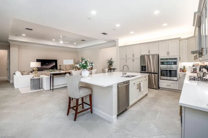 Kitchen featuring light tile flooring, a tray ceiling, an island with sink, appliances with stainless steel finishes, and sink