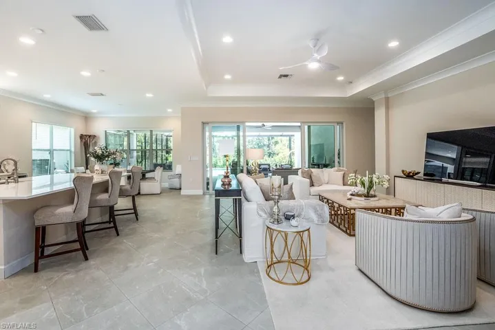 Living room featuring a tray ceiling, crown molding, ceiling fan, and light tile floors