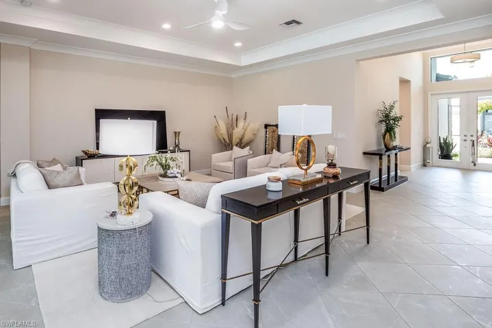 Tiled living room featuring ceiling fan, a tray ceiling, and crown molding