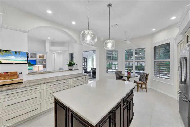 Dual tone kitchen featuring dual tone cabinets, light stone countertops, a kitchen island, stainless steel fridge, and decorative light fixtures