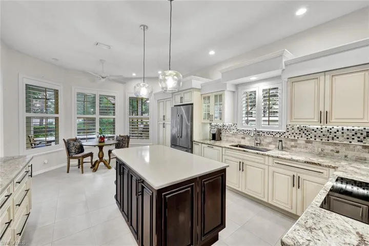 Kitchen featuring two tone cabinets, a kitchen island, high end fridge, light stone counters, and tasteful backsplash