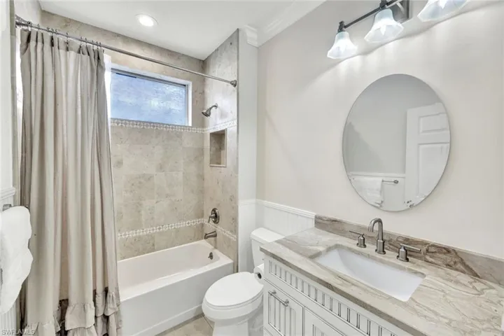 Bathroom featuring vanity, shower / tub combo, crown molding, and a wainscoted wall