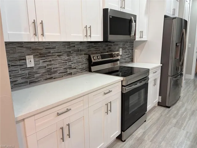 Kitchen featuring appliances with stainless steel finishes, white cabinetry, tasteful backsplash, light stone countertops, and light wood-style flooring