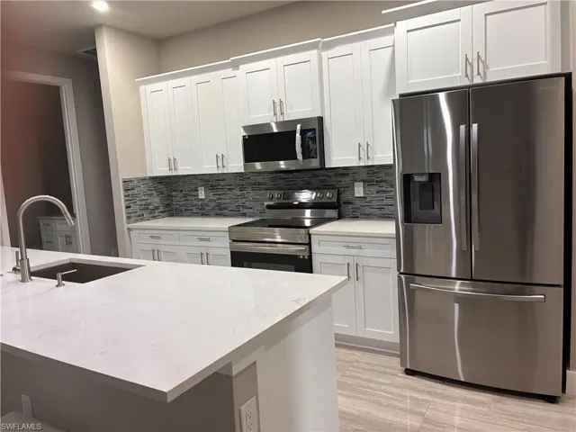 Kitchen featuring appliances with stainless steel finishes, tasteful backsplash, white cabinetry, and light stone countertops