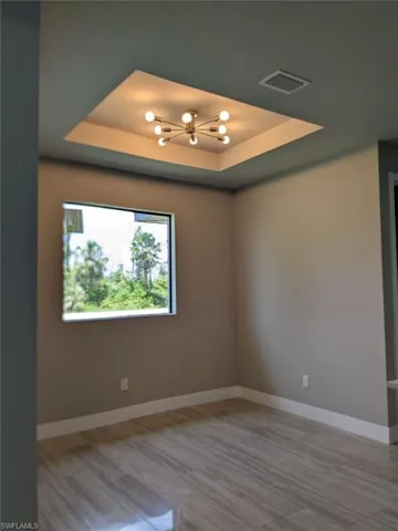 Spare room with a chandelier, a tray ceiling, and wood finished floors